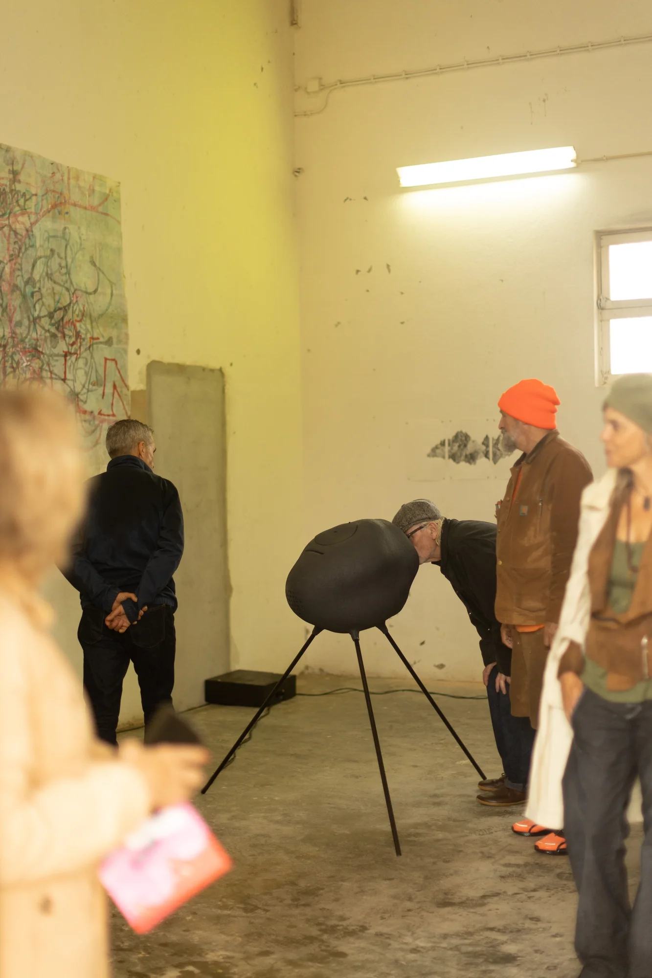 Visitantes debruçam-se para ouvir uma escultura sonora na exposição Filling Tanks with Ghosts