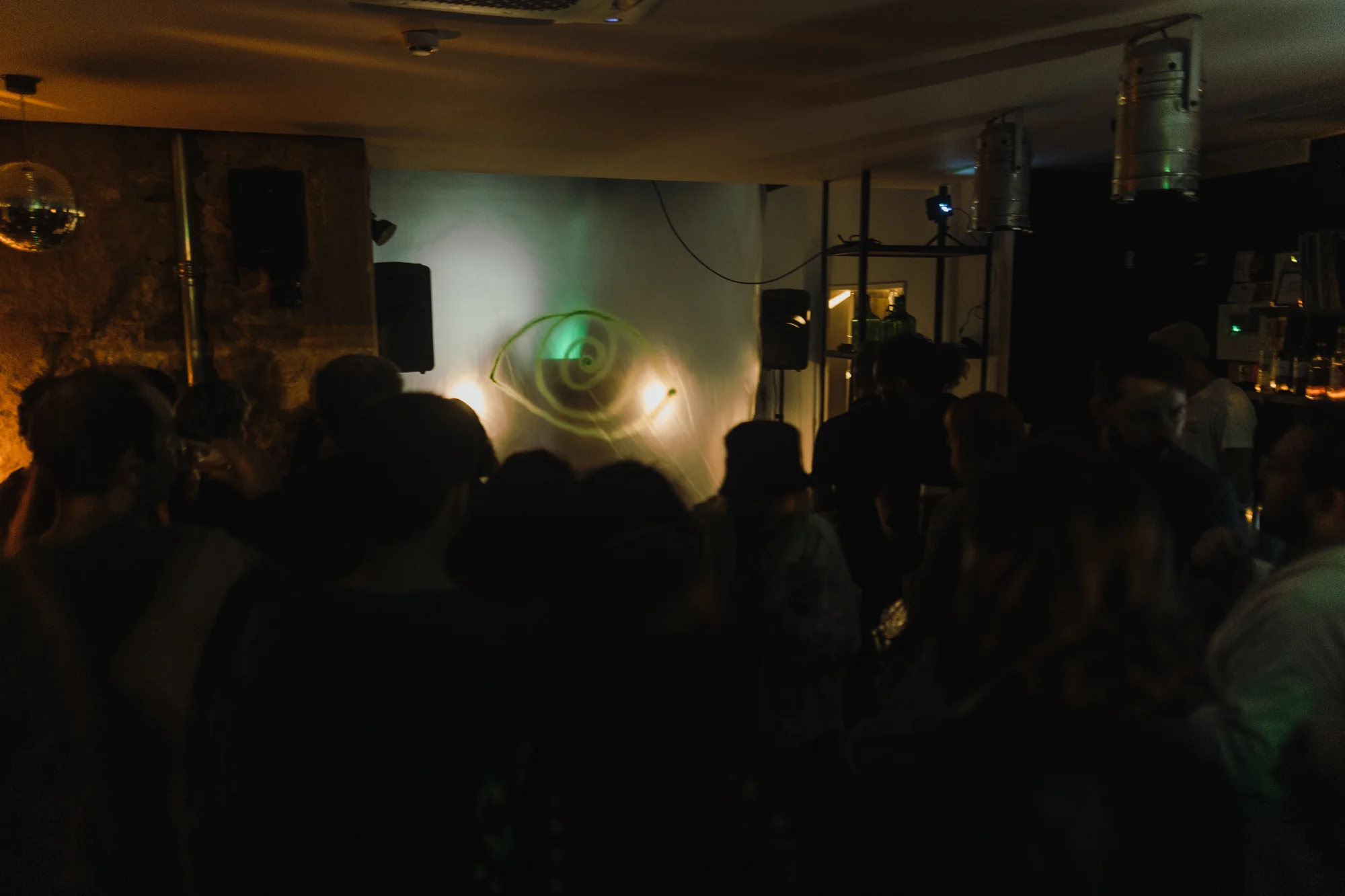 Multidão em silhueta observa a projeção laser em espiral da instalação a E(y)e cult