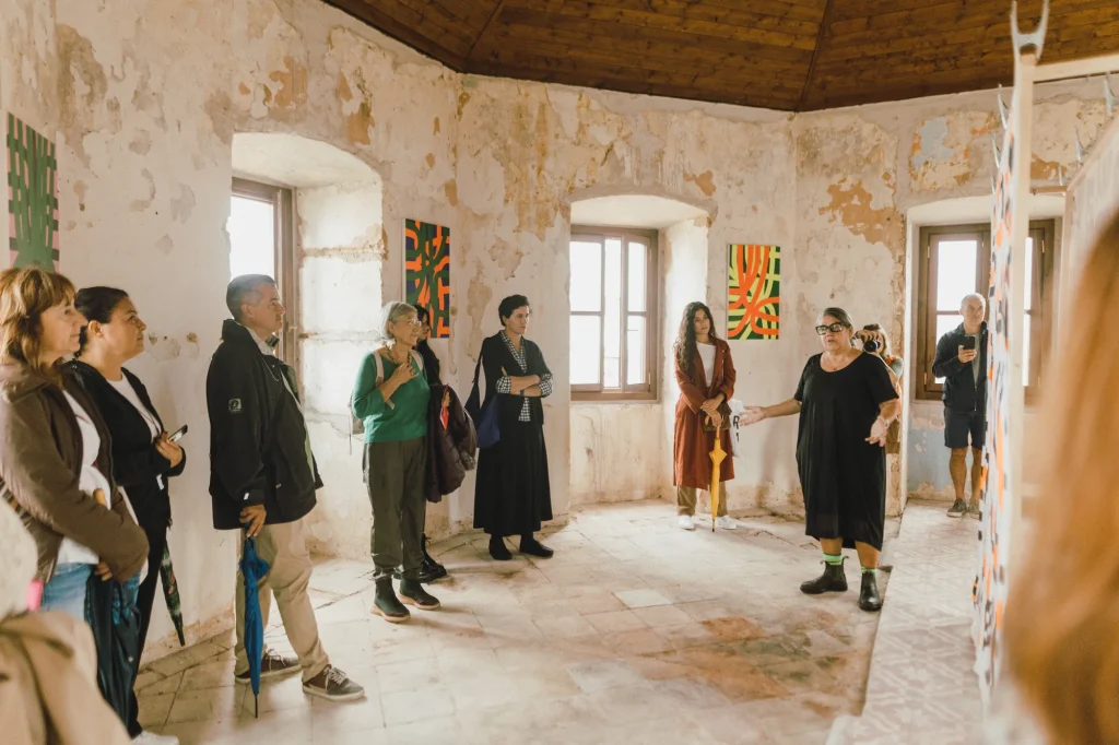 Guia tem a atenção total de um grupo diverso numa sala de galeria iluminada pelo sol